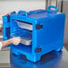 A man using a Cambro navy blue front loading food pan carrier to transport metal food pans.