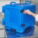 A hand opening a navy blue Cambro insulated food pan carrier.