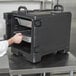 A man putting a food tray in a black Cambro Ultra Pan Carrier.