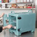 A man opening a blue Cambro food pan carrier.