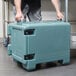 A man using a Cambro Ultra Pan Carrier in slate blue to hold large plastic containers.