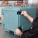 A man opening a Cambro slate blue front loading insulated food pan carrier.