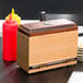 A brown rectangular lid on a wooden box with a bottle of ketchup.