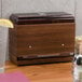 A wooden box with a Vollrath Straw Boss lid on a counter with a glass of water with a lemon wedge.