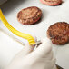 A person using a Cooper-Atkins yellow and white tool to check the temperature of a burger.