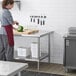 A woman in a chef's uniform cutting vegetables on a Regency stainless steel work table with an undershelf.