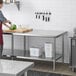 A woman in a red apron preparing food on a Regency stainless steel work table with undershelf.