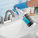 A hand in a blue glove uses a spray bottle of 3M TB Quat Disinfectant to clean a white sink.