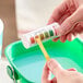 A hand holding a test tube with a paper strip over it in a green and white Noble Chemical container.