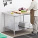 A man in a chef's uniform cutting vegetables on a Regency stainless steel work table with undershelf.