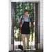 A man wearing a black apron holding a broom and standing in front of a black rectangular mesh strip door.