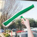 A hand holding Unger ThePad StripWasher with a green and white brush cleaning a window.