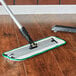 A 3M green wet mop pad with a black handle on a wood floor.