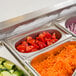 A Vollrath stainless steel oval pan with sliced tomatoes on a counter in a row of food trays.