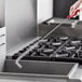 A hand with a red handle using a Carlisle Sparta High-Heat Fryer Brush over a stainless steel sink.