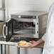 A man in a white shirt and apron cooking food in a Solwave commercial microwave.