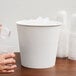 A hand pouring ice from a white Lavex paper ice bucket into a plastic cup.