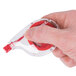 A hand holding a red and clear Universal correction tape dispenser.