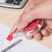 A hand holding a red Universal correction tape dispenser over paper with a keyboard.