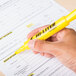 A hand using an Avery yellow chisel tip highlighter to mark a paper.