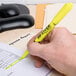 A hand using an Avery yellow pen style highlighter to highlight a paper.