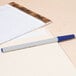 A blue Universal oil-based ballpoint pen next to a pad of paper.