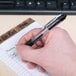 A hand using a Universal One black clear gel pen to write on a piece of paper.