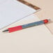 A Universal red retractable rollerball gel pen on a table with a notepad.