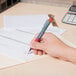 A hand holding a Universal red medium point gel pen and writing on a piece of paper.