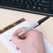 A hand holding a Universal black fine point ballpoint pen and writing on a notebook.