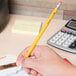 A hand holding a Universal yellow barrel pencil writing on a piece of paper.