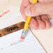 A hand holding a Universal yellow HB lead pencil over a piece of paper.