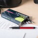 A box of Universal One red medium point retractable ballpoint pens on a desk with one pen next to it.