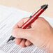 A hand holding a Universal One red retractable ballpoint pen over a document.