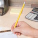 A hand holding a Universal yellow woodcase pencil writing on a piece of paper.