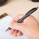 A hand using a Universal One Comfort Grip blue ballpoint pen to write on a notepad.