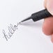 A hand writing "hello" in cursive with a Universal One Comfort Grip Black Retractable Ballpoint Pen.