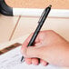 A hand holds a Universal One Comfort Grip black ballpoint pen over a piece of paper.