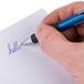 A hand writing "hello" on paper with a Universal One blue ballpoint pen.