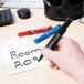 A hand using a blue Avery Marks-A-Lot permanent marker to write on paper.