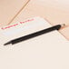 A black Universal One Comfort Grip ballpoint pen writing on a piece of paper.