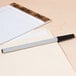 A Universal black medium point oil-based ballpoint pen on a pad of lined paper.