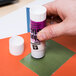 A hand holding a purple tube of Avery Disappearing Color glue.
