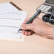 A hand holding a Universal black medium point gel pen and writing on a piece of paper.