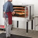 A man in an apron standing in front of a Cooking Performance Group natural gas convection oven.