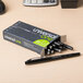 A box of Universal black medium point rollerball pens on a table.