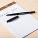 A Universal One black medium point rollerball pen on a pad of paper.