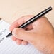 A hand holding a Universal One black medium point rollerball pen and writing.