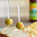 A sandwich with chips and a green olive on a plate with a Royal Paper clear plastic prism food pick.