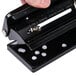A hand holding a Universal black countertop hole punch with 2 holes in a sheet of paper.